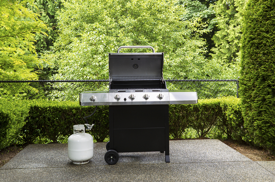 Horizontal photo of large barbeque cooker with lid up on concrete outdoor patio with woods background